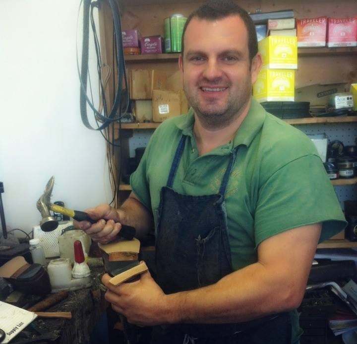 Jose Santiago smiling at his workbench, holding a hammer and a shoe