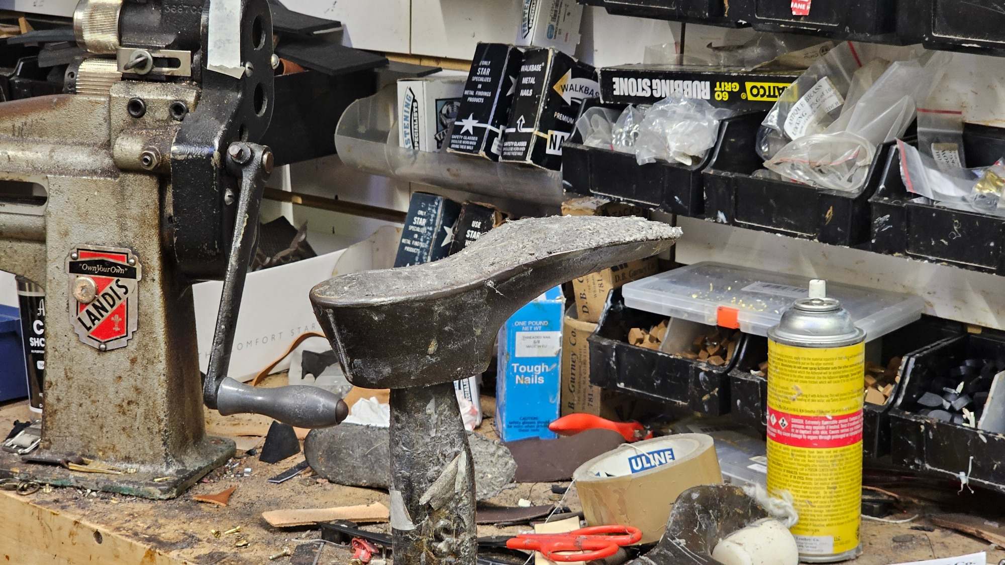 A cobbler’s iron shoe last on the Magic Shoe repair bench beside the Landis machine, tools, and repair supplies